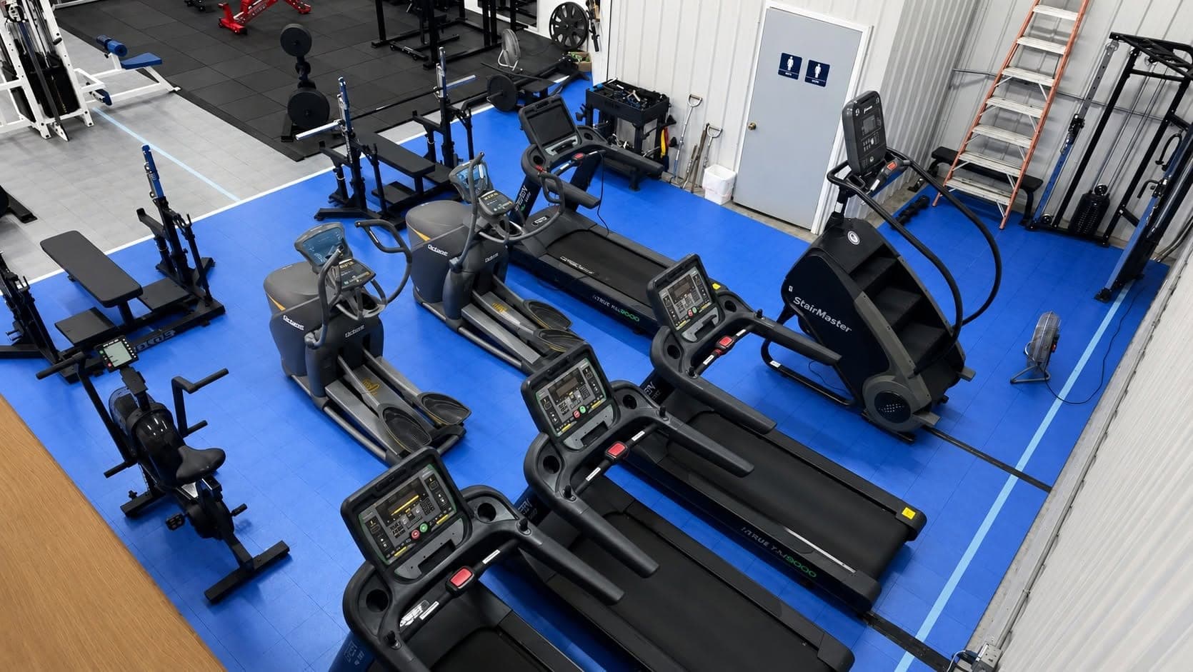 Treadmills, ellipticals and a StairMaster on blue flooring at Blue Water Fitness