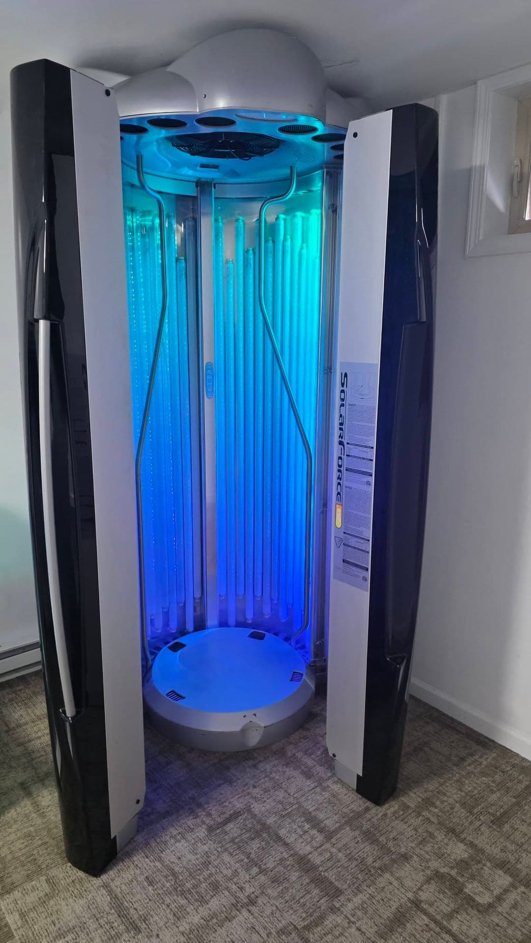 The Level 5 stand-up tanning booth at Blue Water Fitness, lit blue